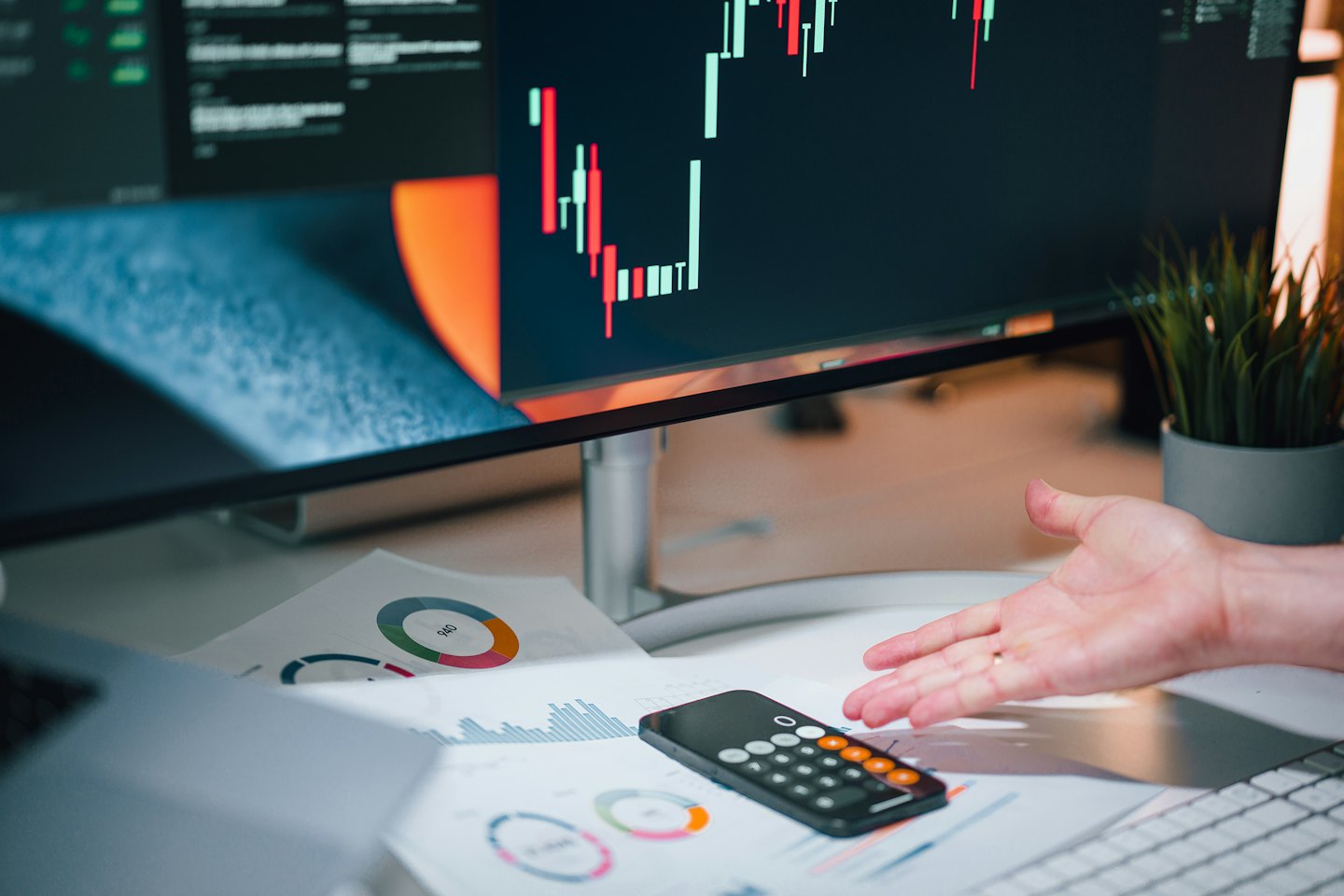 Hand gesturing over financial charts on a desk.